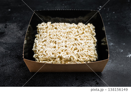 Raw wheat instant noodle brick served in bowl with seasoning powder on dark backdrop Asian pantry staple closeup top view Raw wheat instant noodle brick served in bowl with seasoning powder on dark backdrop Asian pantry staple closeup top view 138156149