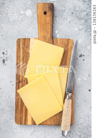 Stack of semi hard yellow cheese slices on rustic wooden cutting board, copy space on gray stone background, dairy ingredient Stack of semi hard yellow cheese slices on rustic wooden cutting board, copy space on gray stone background, dairy ingredient 138156163