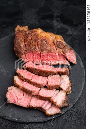 Sliced beef chuck eye roll steak cooked medium rare with juicy texture. Gourmet beef meat with salt on dark stone background. 138156168