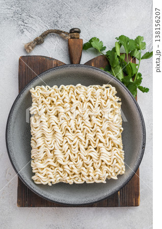 Raw wheat instant noodle brick in gray bowl on light surface with copy space minimal cooking ingredient flat lay. Raw wheat instant noodle brick in gray bowl on light surface with copy space minimal cooking ingredient flat lay. 138156207
