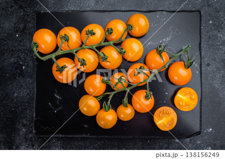 Organic orange cherry tomatoes whole and sliced on slate serving board, dramatic dark food composition with copy space Organic orange cherry tomatoes whole and sliced on slate serving board, dramatic dark food composition with copy space 138156249