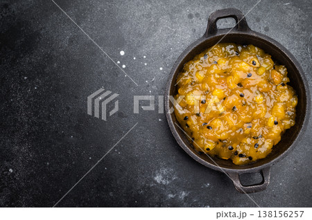 Mango and passion fruit sauce in cast iron pan on dark background, gourmet tropical fruit reduction with glossy texture 138156257