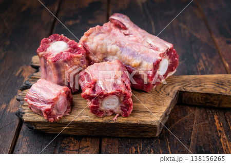 Lamb oxtail sections ready for cooking with herbs on wooden cutting board, overhead composition on dark wood surface 138156265