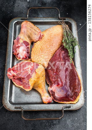 Uncooked duck breast and leg cuts on tray with herbs. Poultry game meat ingredient for cooking gastronomy overhead with copy space. 138156274
