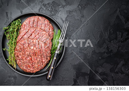 Fresh raw minced beef and lamb cutlets in plate with herbs. Flat lay on dark stone background for barbecue themes. 138156303