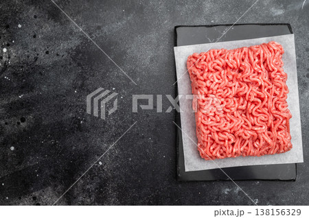 Raw minced beef ground meat portion on parchment paper on slate board with dark background and copy space Raw minced beef ground meat portion on parchment paper on slate board with dark background and copy space 138156329