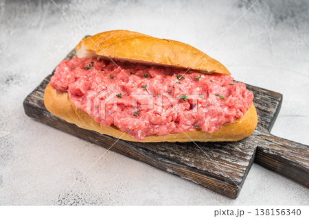 Cannibal sandwich with raw minced beef served on bread roll on rustic wooden board on light background Cannibal sandwich with raw minced beef served on bread roll on rustic wooden board on light background 138156340