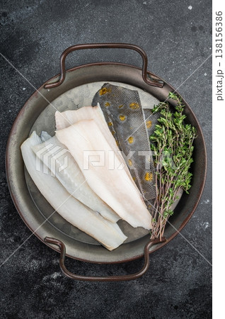 Raw flounder flatfish fillets with skin and thyme on metal tray on dark background fresh seafood ingredient. Raw flounder flatfish fillets with skin and thyme on metal tray on dark background fresh seafood ingredient. 138156386