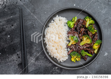 Beef and broccoli stir fry with rice and sesame seeds served on black plate with chopsticks on dark background Beef and broccoli stir fry with rice and sesame seeds served on black plate with chopsticks on dark background 138156398