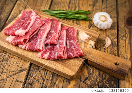 Luxury marbled beef short plate slices resembling wagyu texture on wooden board with herbs, raw angus meat preparation concept Luxury marbled beef short plate slices resembling wagyu texture on wooden board with herbs, raw angus meat preparation concept 138156399