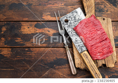 Raw beef flank steak with strong muscle grain on butcher cleaver and wooden board rustic meat preparation scene Raw beef flank steak with strong muscle grain on butcher cleaver and wooden board rustic meat preparation scene 138156405