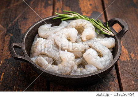 Raw peeled shrimp prawn and rosemary in a dark cast iron skillet on a rustic wooden background. Top view with copy space for recipe or menu. Raw peeled shrimp prawn and rosemary in a dark cast iron skillet on a rustic wooden background. Top view with copy space for recipe or menu. 138156454