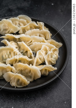 Tasty steamed gyoza wontons arranged on a black plate over concrete background. Authentic asian appetizer for menus and culinary projects. Tasty steamed gyoza wontons arranged on a black plate over concrete background. Authentic asian appetizer for menus and culinary projects. 138156463