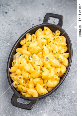 Creamy mac and cheese in a black cast iron skillet, resting on a rustic wooden board against a gray background. 138156467