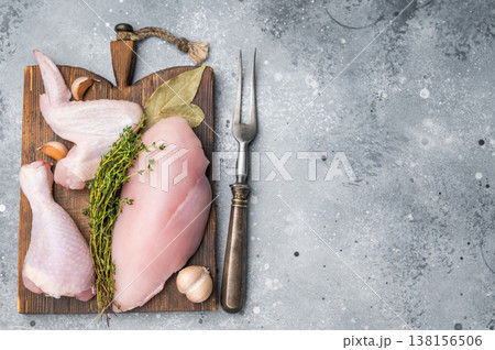 Fresh raw chicken parts (breast, wing, leg) on a rustic cutting board with herbs, spices, and meat fork on a gray stone surface. Copy space. Fresh raw chicken parts (breast, wing, leg) on a rustic cutting board with herbs, spices, and meat fork on a gray stone surface. Copy space. 138156506