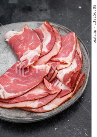 Traditional Italian salumi coppa with marbling served on a gray plate with salt on dark stone background great for charcuterie imagery. Traditional Italian salumi coppa with marbling served on a gray plate with salt on dark stone background great for charcuterie imagery. 138156508