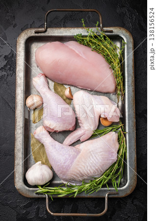 Raw chicken assortment: breast, leg, drumstick, and wing with fresh herbs and garlic on a metal tray, on a dark textured background. Copy space. Raw chicken assortment: breast, leg, drumstick, and wing with fresh herbs and garlic on a metal tray, on a dark textured background. Copy space. 138156524