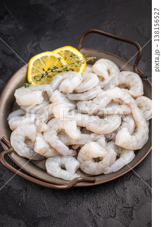 Raw peeled shrimp prawn with lemon and thyme in a metal pan on a textured black background. Maximum contrast with copy space. 138156527
