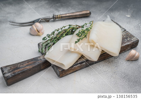 Raw calamari arranged with herbs on weathered wood against a gray stone backdrop ideal for culinary seafood stock concepts. 138156535