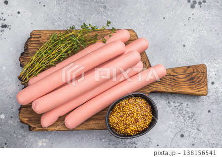 Raw hot dog sausages (frankfurters/wieners) on a cutting board with thyme and mustard on a rustic background. Food preparation concept. Raw hot dog sausages (frankfurters/wieners) on a cutting board with thyme and mustard on a rustic background. Food preparation concept. 138156541