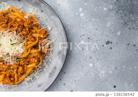 Hearty Italian bolognese pasta topped with minced meat sauce and grated cheese on a gray ceramic plate against stone background. Hearty Italian bolognese pasta topped with minced meat sauce and grated cheese on a gray ceramic plate against stone background. 138156542