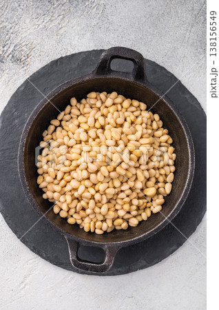 Raw pine nuts arranged in a small cast iron dish on a slate plate over a light textured surface creating a clean contrast for recipe and food visuals Raw pine nuts arranged in a small cast iron dish on a slate plate over a light textured surface creating a clean contrast for recipe and food visuals 138156549