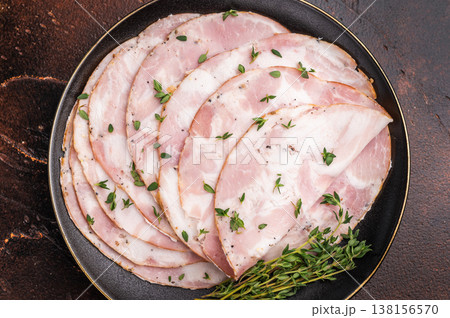 Slices of Italian Pancetta Arrotolata with thyme on a black plate, next to a vintage fork on a dark brown background. 138156570
