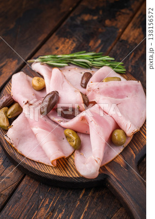 Cured pork slices lonza with olives and rosemary on a rustic wooden board over dark aged wood creating a simple and commercial food background. 138156572