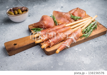 Gourmet Italian Antipasto with prosciutto crudo, grissini breadsticks, and olives on a rustic wooden board. Top view with copy space. 138156576