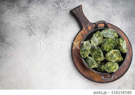 Overhead shot of frozen spinach blocks in a cast iron skillet on a wooden board. Grey textured background with copy space. 138156580