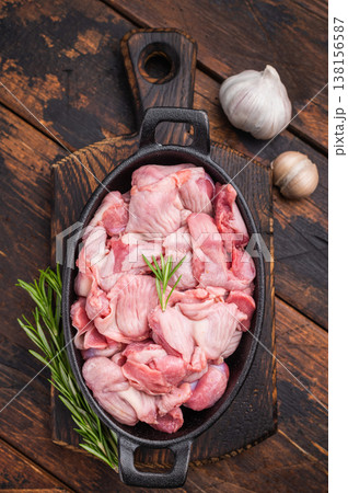 Fresh poultry offal in a cast iron dish, accompanied by aromatic herbs and garlic on a wooden surface 138156587