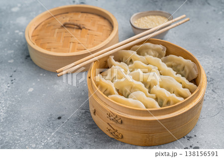 Steamed Asian dumplings mandu served in bamboo steamer on concrete background with chopsticks perfect for dim sum menus. Steamed Asian dumplings mandu served in bamboo steamer on concrete background with chopsticks perfect for dim sum menus. 138156591