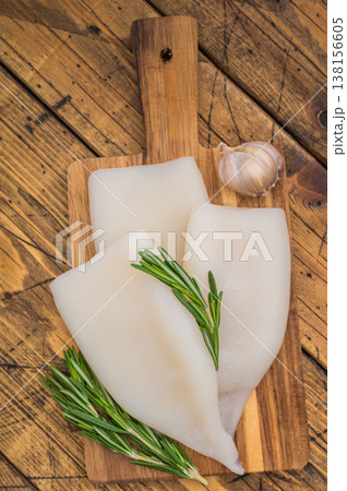 Raw calamari and fresh rosemary on vintage wood board captured for culinary design seafood menus and Mediterranean style visuals Raw calamari and fresh rosemary on vintage wood board captured for culinary design seafood menus and Mediterranean style visuals 138156605