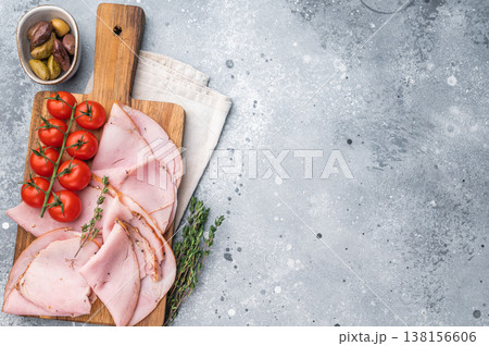 Sliced Prosciutto cured pork, cherry tomatoes and thyme displayed on a wooden cutting board with a light napkin on a textured gray backdrop. Sliced Prosciutto cured pork, cherry tomatoes and thyme displayed on a wooden cutting board with a light napkin on a textured gray backdrop. 138156606
