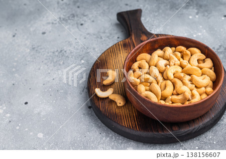 Cashew nuts in a wooden bowl placed on a rustic board against a textured grey background creating a warm natural food scene for culinary stock Cashew nuts in a wooden bowl placed on a rustic board against a textured grey background creating a warm natural food scene for culinary stock 138156607