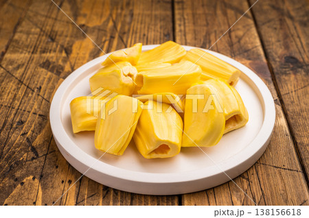 Sweet, golden yellow jackfruit pods (bulbs) served on a white plate on a rustic wooden table. Fresh, tropical fruit snack. Sweet, golden yellow jackfruit pods (bulbs) served on a white plate on a rustic wooden table. Fresh, tropical fruit snack. 138156618