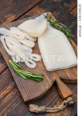 Cleaned squid fillets and rings on textured wood board with rosemary and garlic perfect seafood setup for culinary themes. 138156620