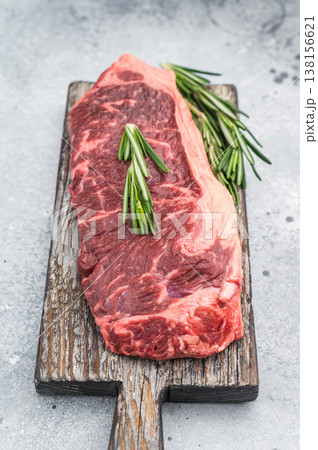 Premium New York steak raw and marbled with rosemary placed on rustic board on bright stone background great for gourmet cooking concepts 138156621