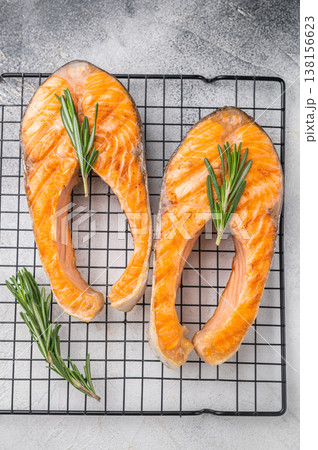 Two cooked salmon slices with herbs resting on a metal grid against a soft gray surface for fresh clean modern food styling. 138156623
