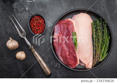 Raw duck breasts skin on and skinless with rosemary and thyme in black plate on dark stone background ideal for gourmet poultry stock images. Raw duck breasts skin on and skinless with rosemary and thyme in black plate on dark stone background ideal for gourmet poultry stock images. 138156626