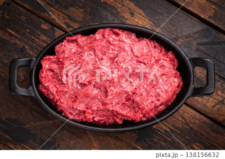 Raw ground wild game meat (venison/boar) in a black skillet on a rustic wooden board, seasoned with fresh thyme and peppercorns. Raw ground wild game meat (venison/boar) in a black skillet on a rustic wooden board, seasoned with fresh thyme and peppercorns. 138156632