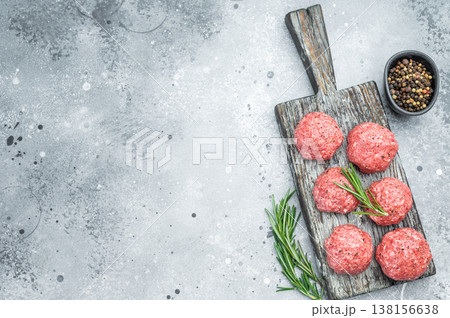 Fresh raw meatballs or frikkadel with rosemary and pepper on rustic wooden board over gray background ideal for cooking, protein and food prep themes. 138156638