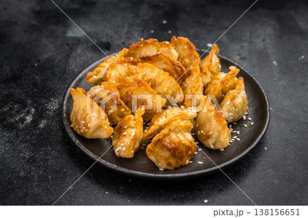 Golden potstickers fried dumplings mandu jiaozi on rustic dark surface Asian snack with crispy texture and sesame topping Golden potstickers fried dumplings mandu jiaozi on rustic dark surface Asian snack with crispy texture and sesame topping 138156651