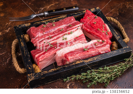 Raw beef short ribs with thyme and fork on a rustic dark background. Excellent for menu design or a butcher shop advertisement. 138156652