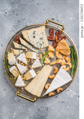 Elegant cheese platter with nuts and herbs presented on a gold tray against a modern gray concrete backdrop for a gourmet look. 138156653