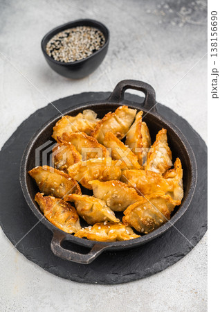Golden fried dumplings jiaozi sprinkled with sesame served in black skillet on bright stone surface perfect Asian snack. Golden fried dumplings jiaozi sprinkled with sesame served in black skillet on bright stone surface perfect Asian snack. 138156690