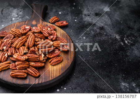 Pecan nuts scattered over a wooden cutting board on a deep textured backdrop giving a natural warm look perfect for recipes and healthy eating themes Pecan nuts scattered over a wooden cutting board on a deep textured backdrop giving a natural warm look perfect for recipes and healthy eating themes 138156707
