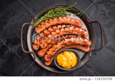 Grilled and cut sausages (frankfurters/wieners) on a rustic platter with mustard sauce and thyme on a dark textured background. Grilled and cut sausages (frankfurters/wieners) on a rustic platter with mustard sauce and thyme on a dark textured background. 138156709