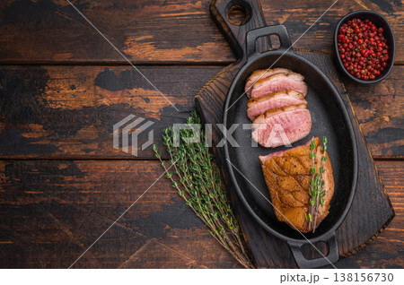 Seared duck breast sliced and served in cast-iron skillet with thyme on rustic wooden background ideal for gourmet food photography. Seared duck breast sliced and served in cast-iron skillet with thyme on rustic wooden background ideal for gourmet food photography. 138156730