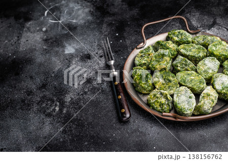 Raw, frozen green vegetable (spinach) portions in a metal serving tray on a dramatic black background. Healthy cooking ingredient. 138156762